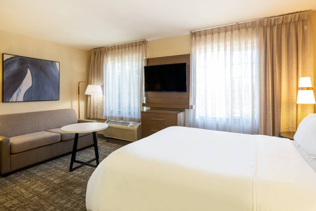 Une chambre d’hôtel avec un lit, un canapé, une télévision, une lampe et des rideaux.