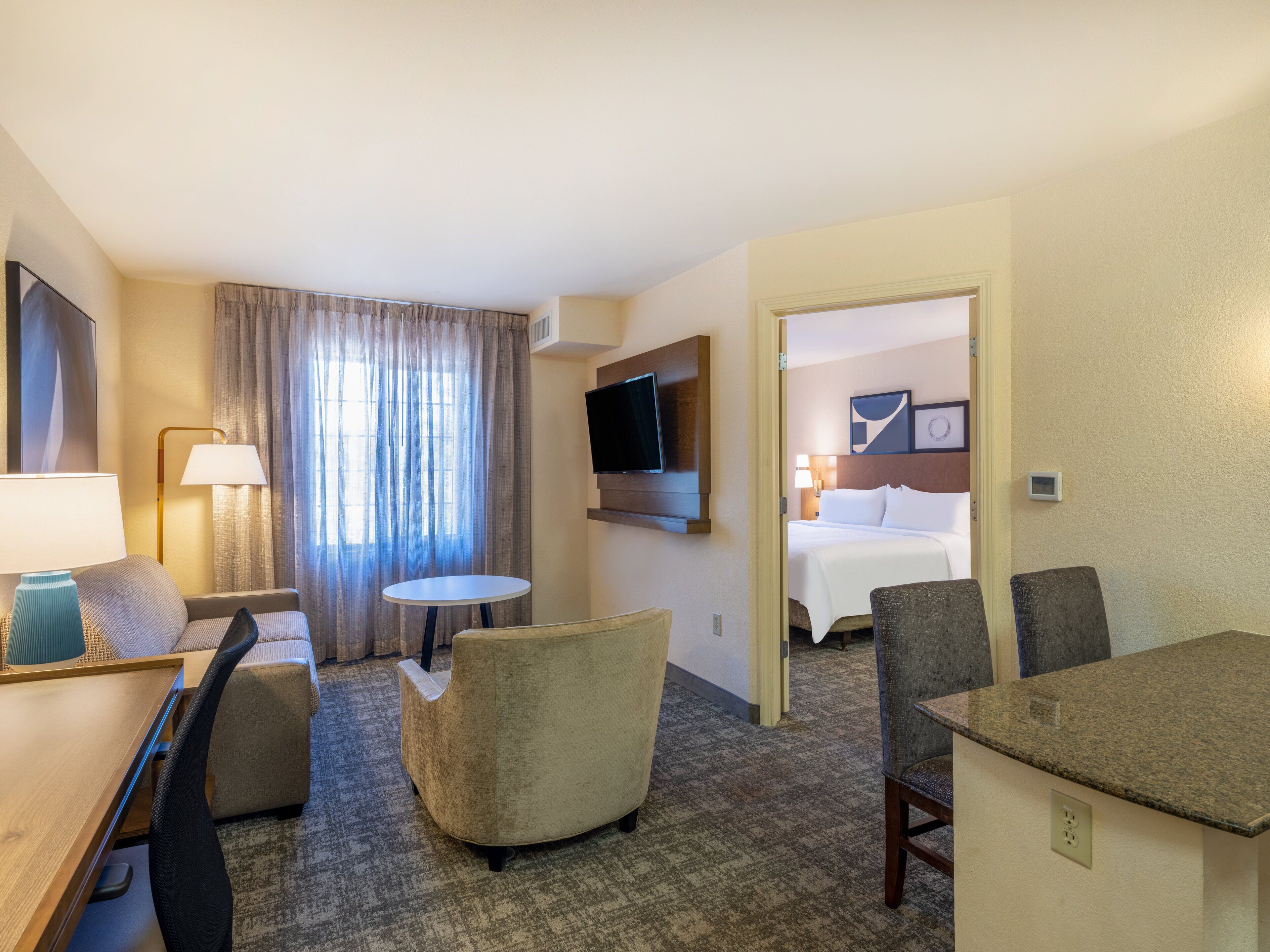 A hotel room with a bed, a desk, a chair, a TV, and a window with curtains.