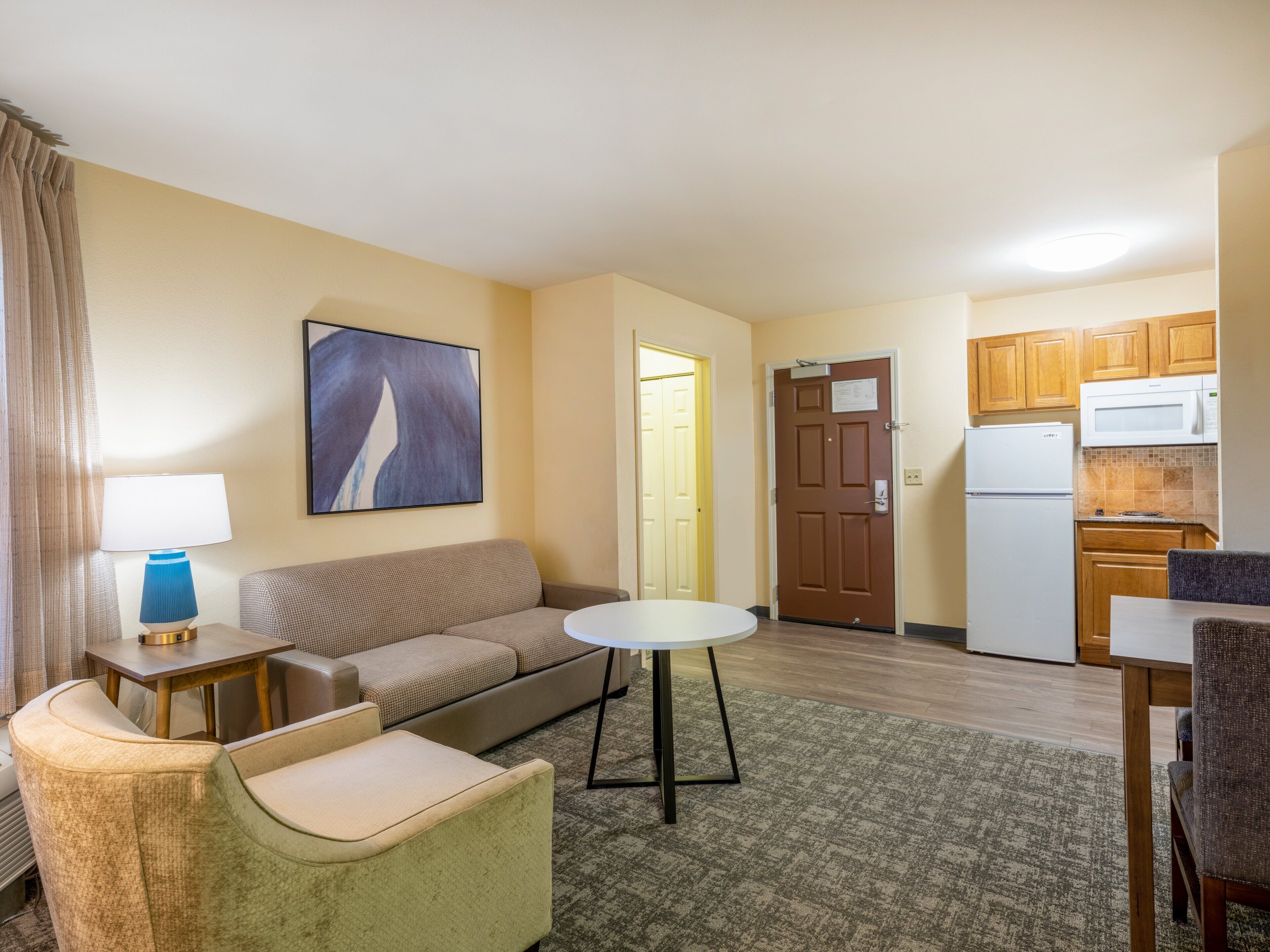 A compact living space with a sofa, armchair, small round table, and a kitchenette in the background.