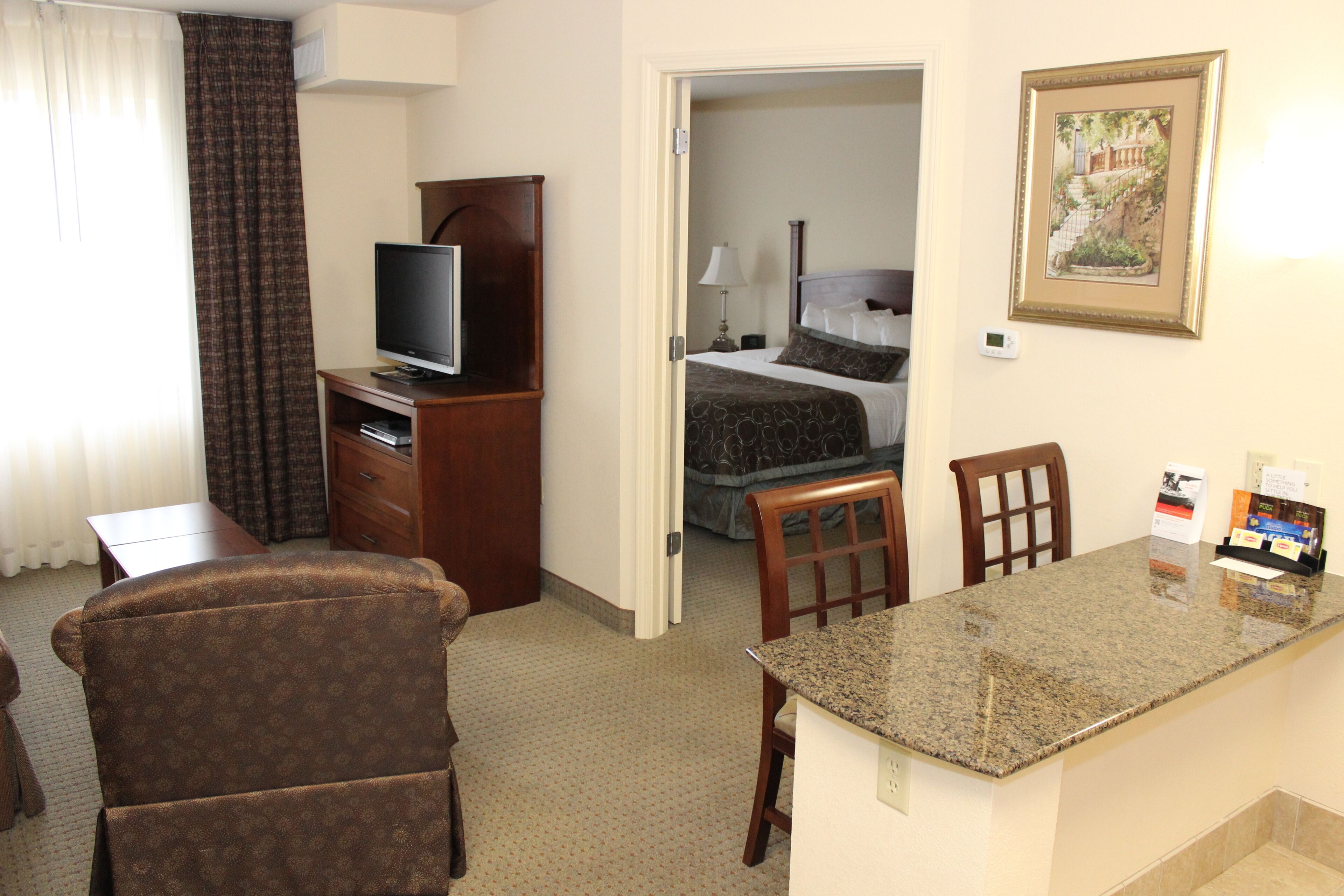 A hotel room with a bed, a desk, a television, and a dining area.