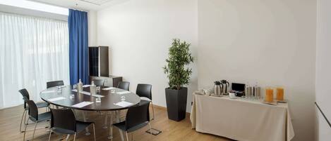 A conference room with a round table, black chairs, a potted plant, and a buffet table with drinks.