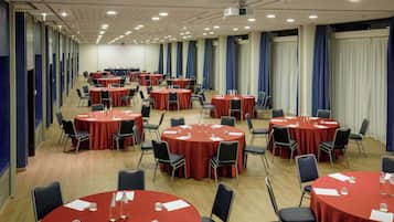 A conference room with multiple round tables, each with chairs and red tablecloths.