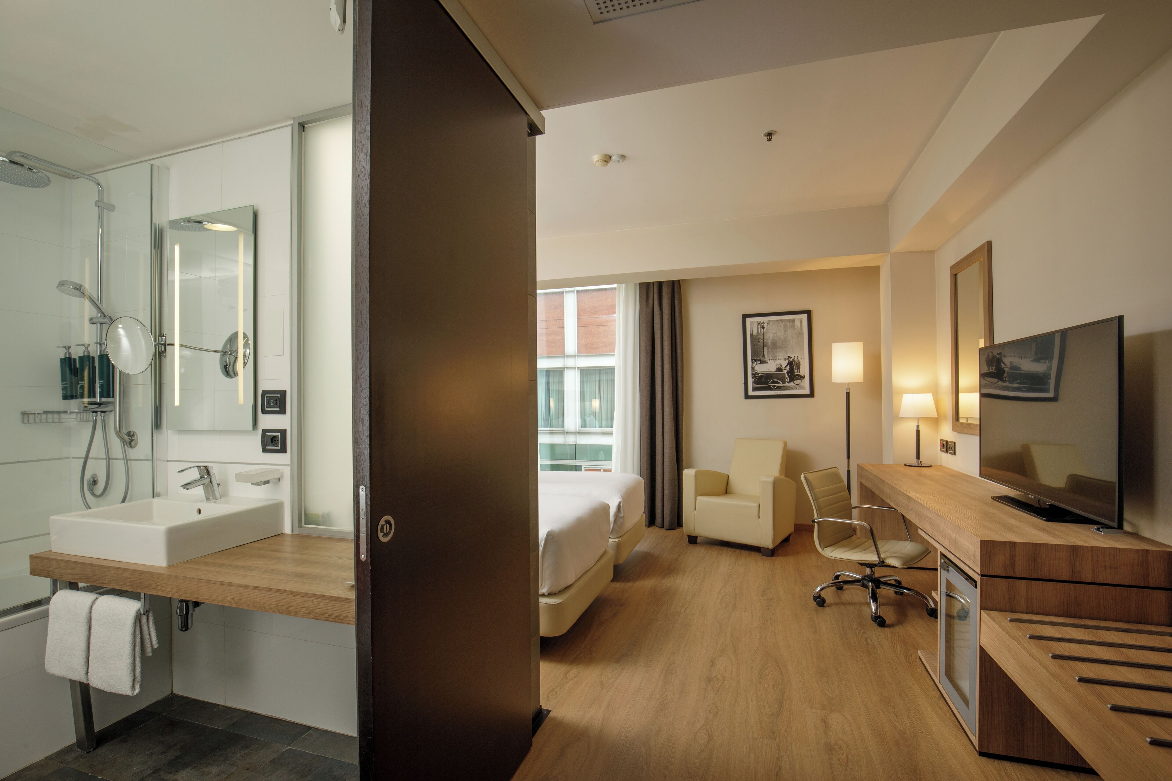 Una camera d'albergo con bagno, un letto, una scrivania con televisore e una sedia.