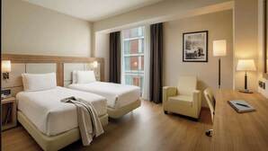 A hotel room with two beds, a desk, a chair, and a window with curtains. - DoubleTree by Hilton Milan (Milan)
