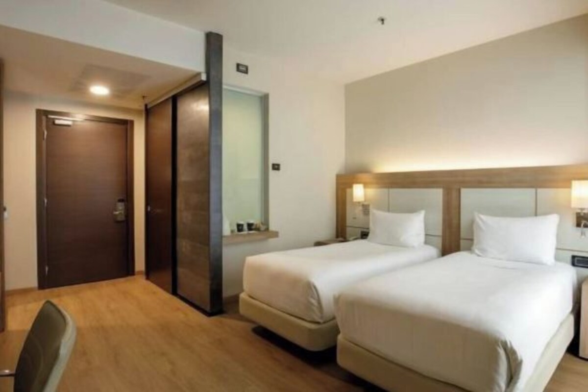 A hotel room with two beds, a wooden floor, a dark door, and a mirror.