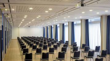 A conference room with rows of chairs, a projector, and large windows with curtains.