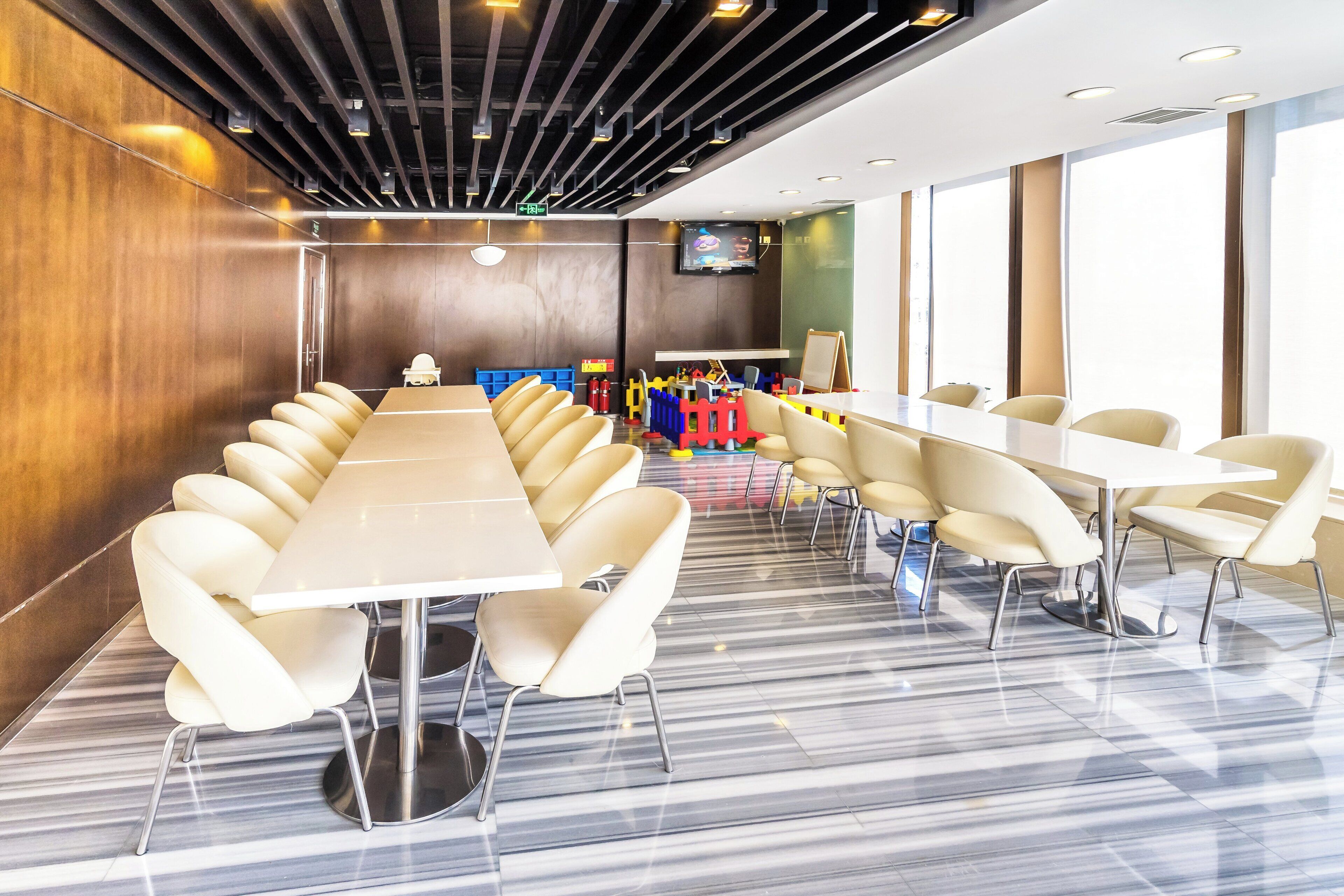 Una sala de conferencias con una larga mesa y sillas, un televisor y un área de juegos infantil con juguetes y un tobogán.