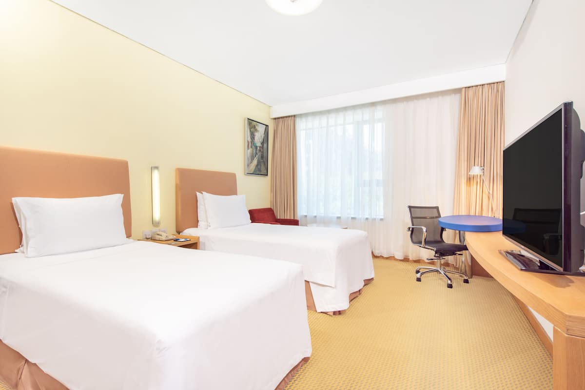 A hotel room with two beds, a desk with a TV, a chair, and a window with curtains.