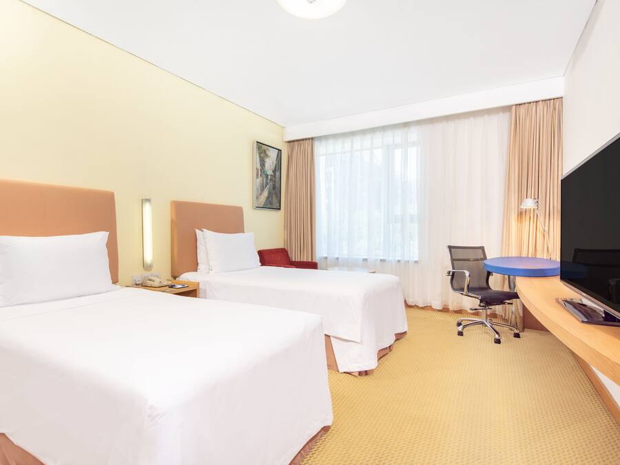 Habitación de hotel con dos camas, un escritorio con televisor, una silla y una ventana con cortinas.