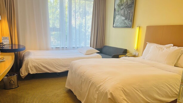 Habitación de hotel con dos camas, un escritorio, una silla, un cesto de basura y un cuadro en la pared.
