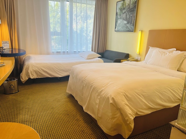 Quarto de hotel com duas camas, uma escrivaninha, uma cadeira, um cesto de lixo e um quadro na parede.