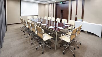 A conference room with a long table, chairs, a projector screen, and a door with an exit sign.