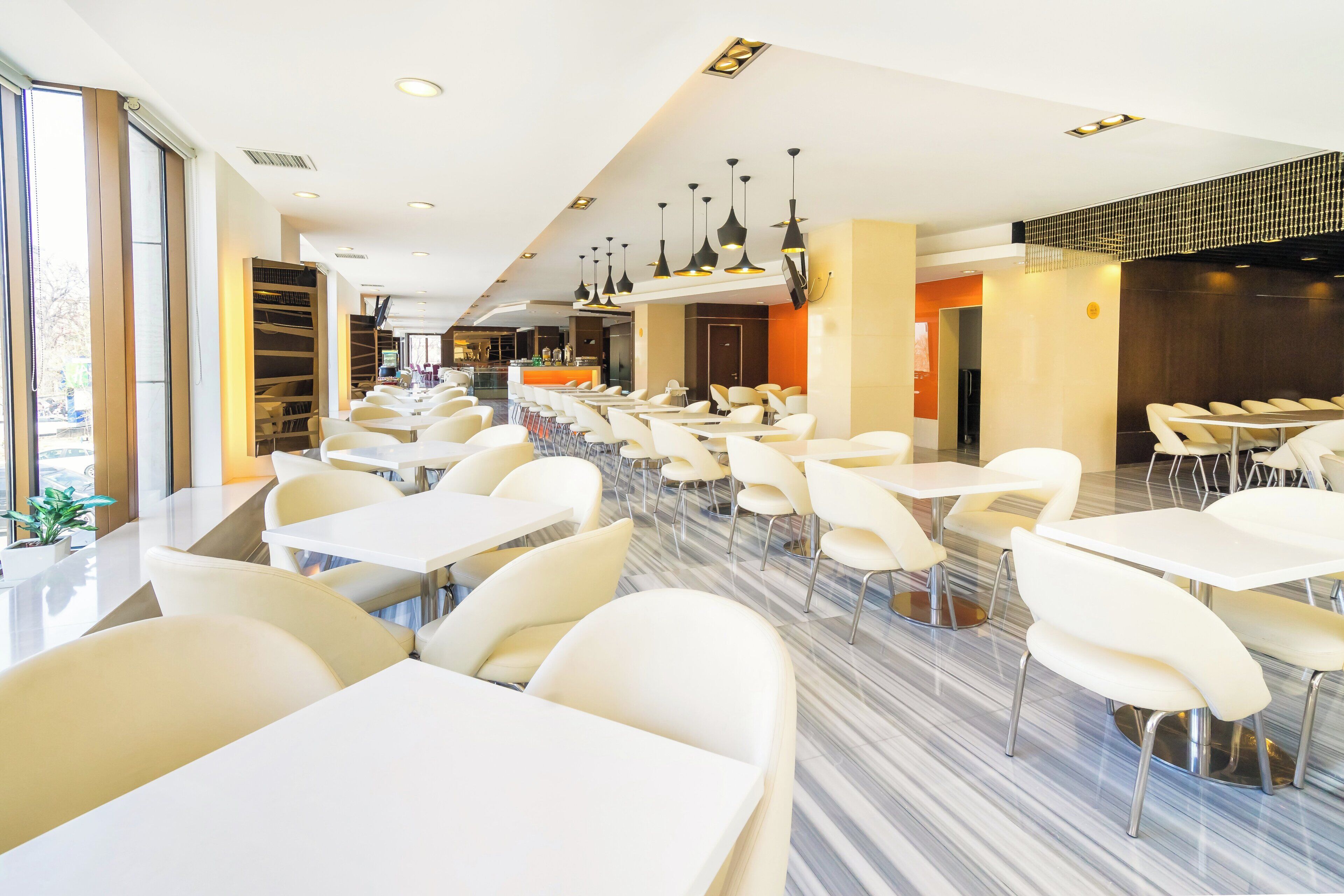 Un espace repas moderne avec des tables et des chaises blanches, un bar et une vue sur l’extérieur.