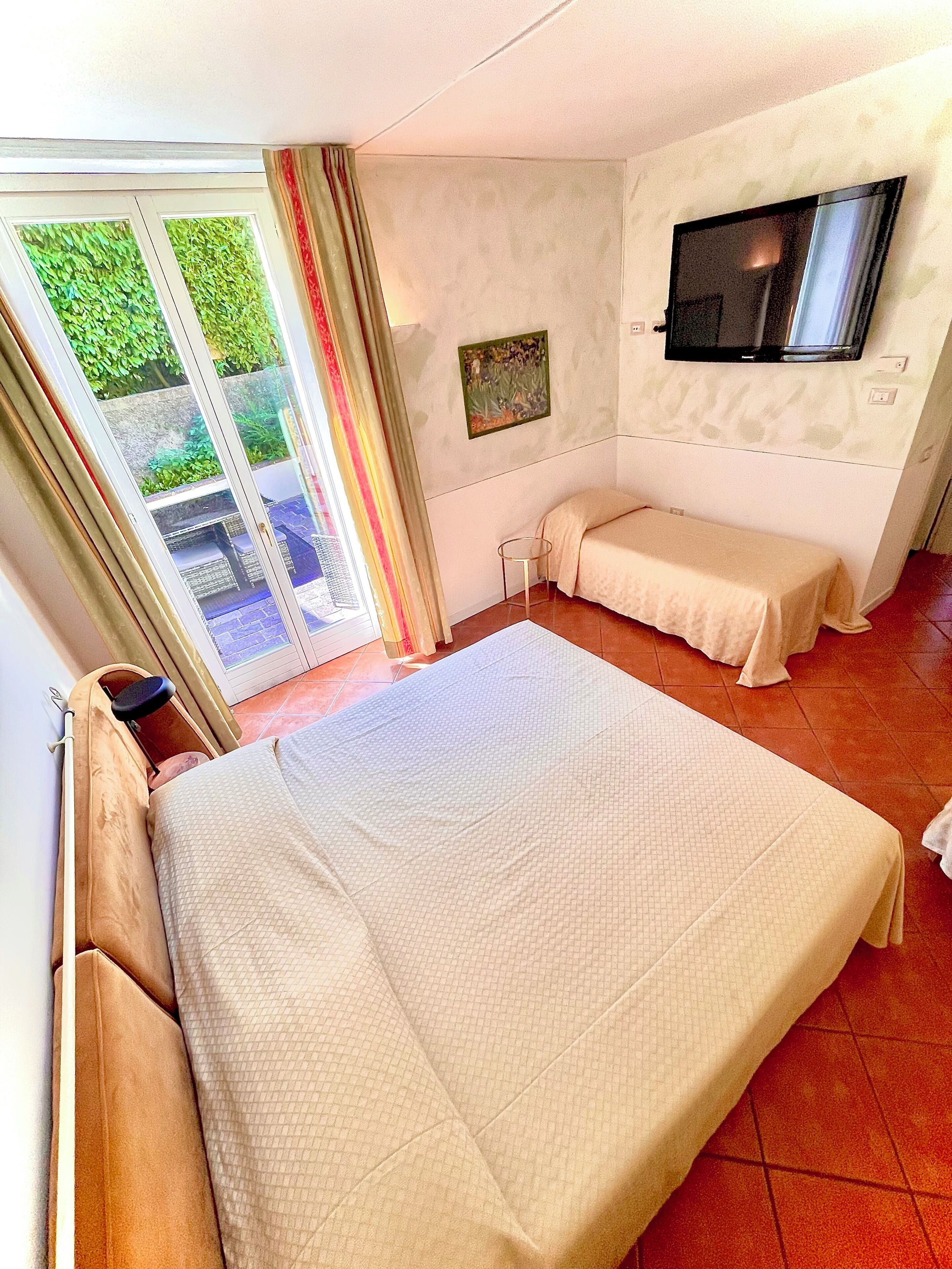 A hotel room with a large bed, a TV mounted on the wall, and a sliding glass door leading to a balcony.
