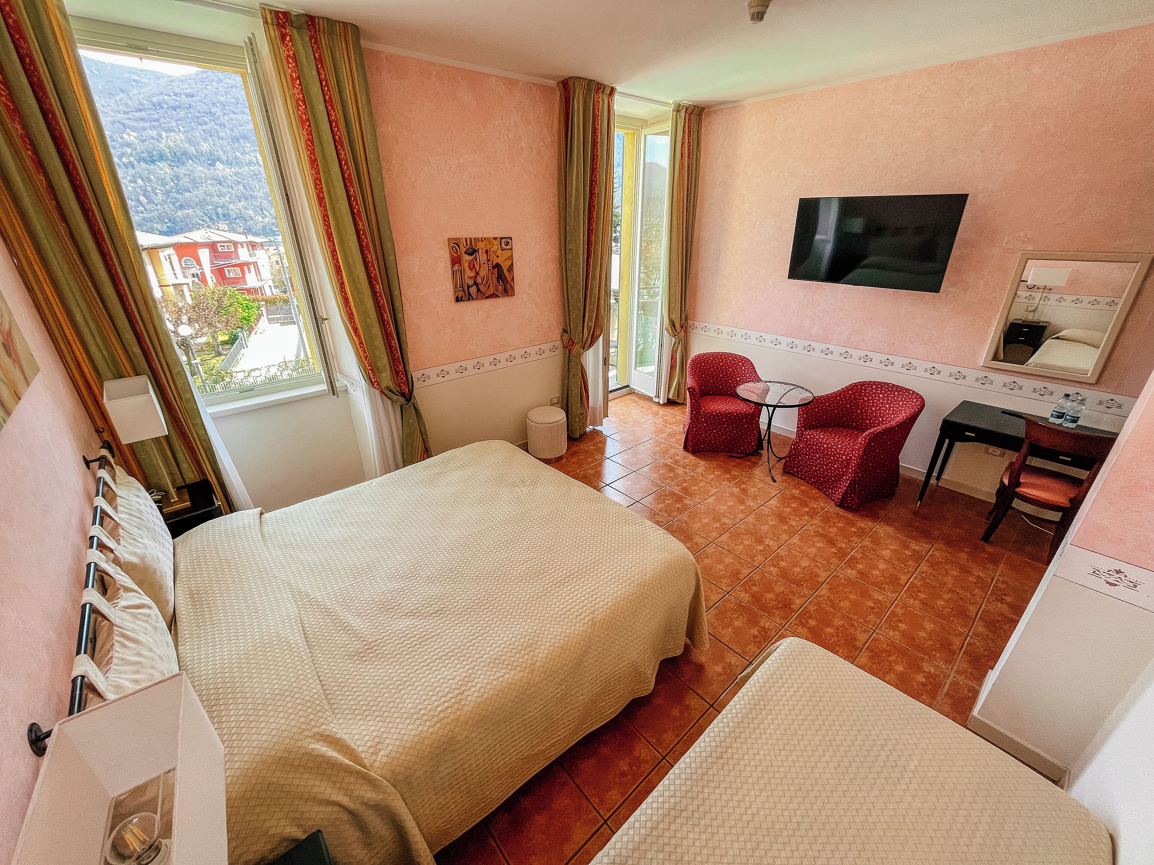A hotel room with a bed, a small table, two chairs, a TV, and a window with curtains.