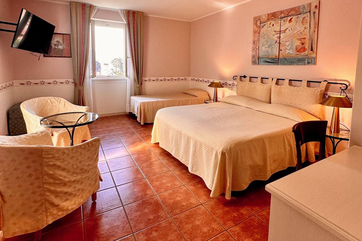 A hotel room with a bed, two bedside tables, a chair, a TV mounted on the wall, and a painting.