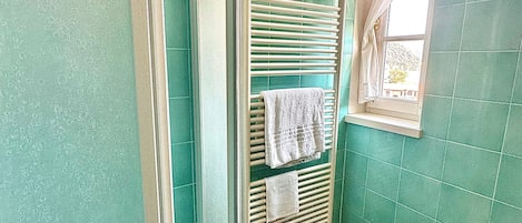 Un baño con azulejos verdes, un lavamanos blanco y un perchero con toallas.