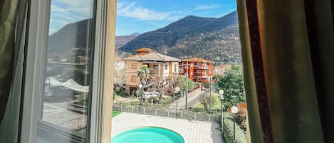 Janela com vista para uma piscina, edifícios e montanhas.