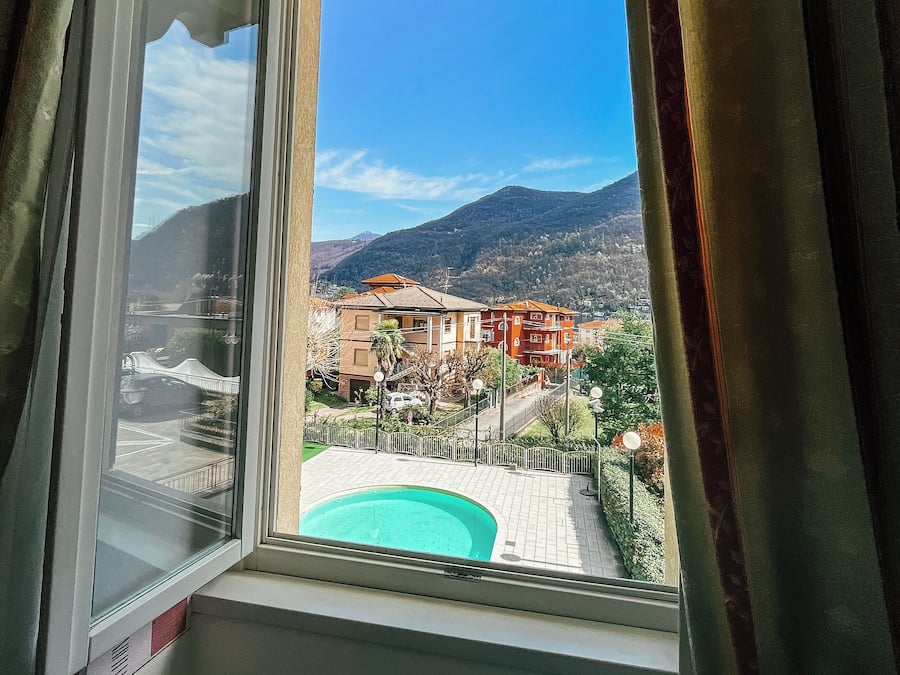 A window with a view of a pool, buildings, and mountains.