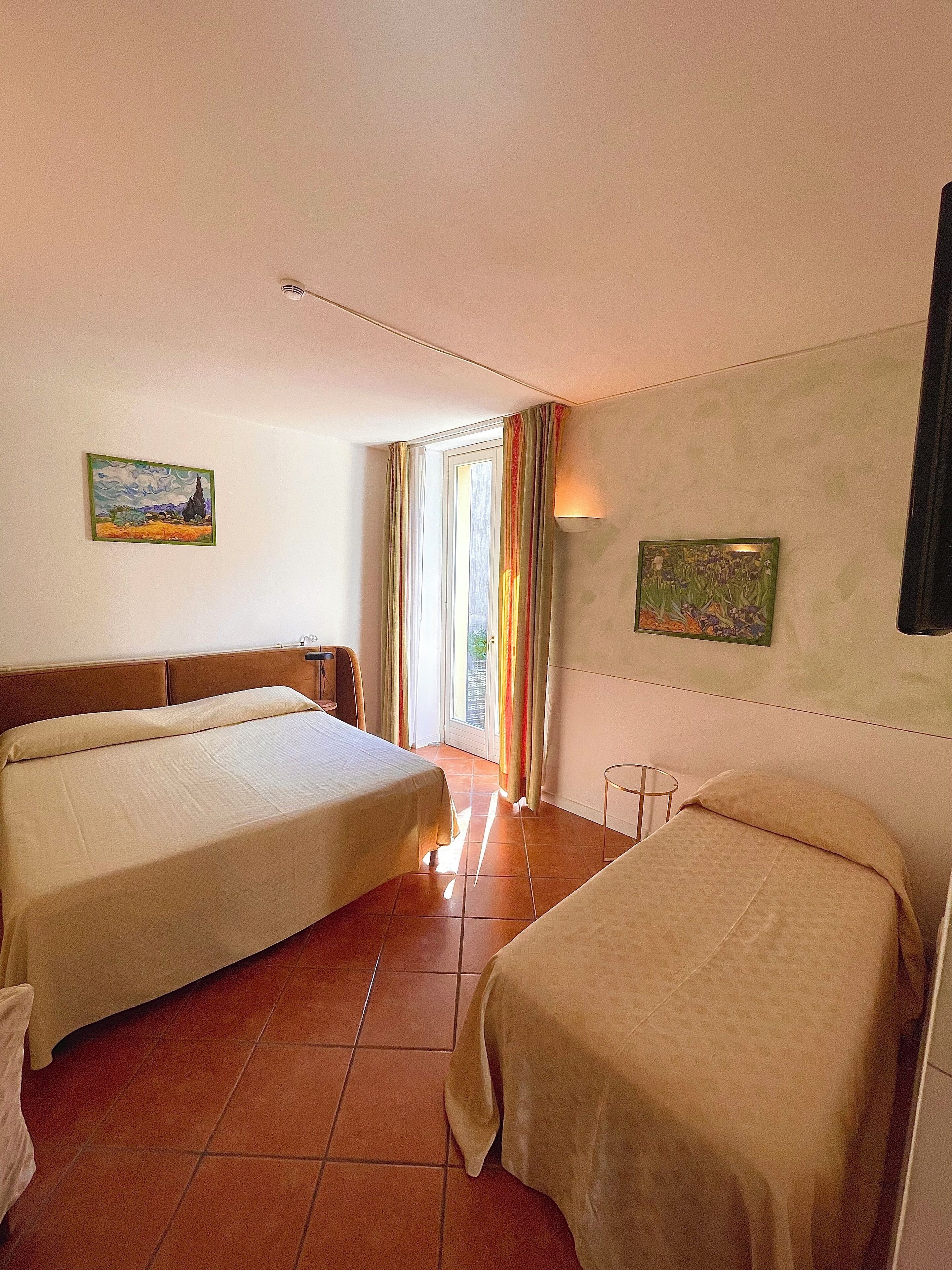 Habitación de hotel con dos camas, una ventana con cortinas y obras de arte en las paredes.