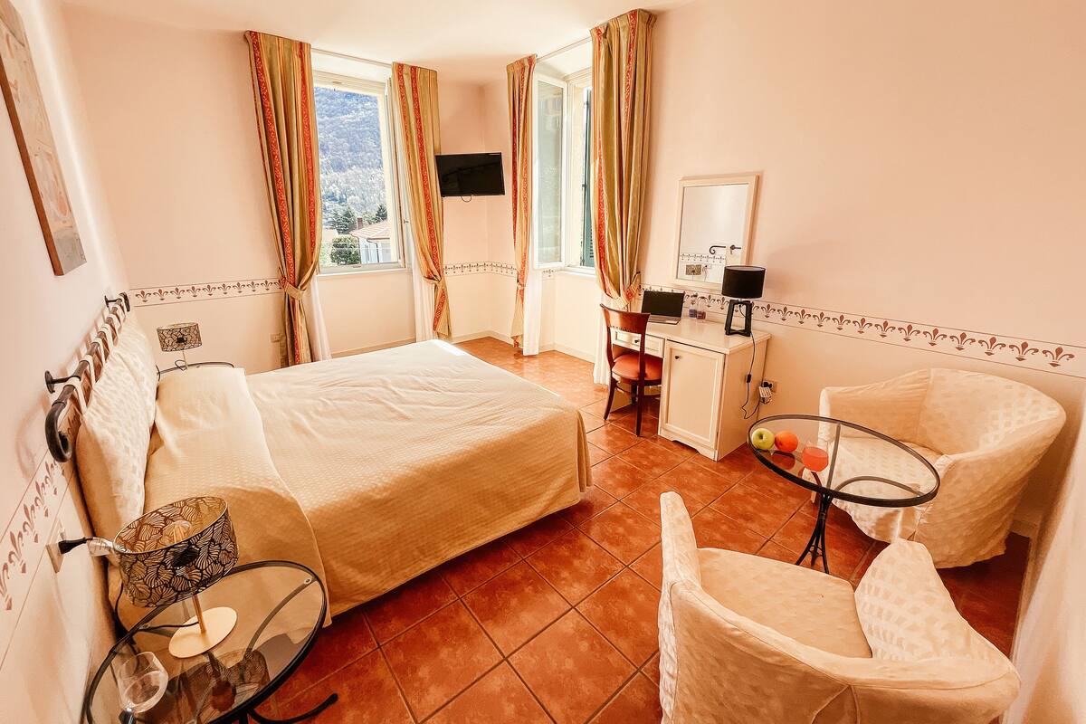 A bedroom with a bed, a desk, a chair, a small table with fruits, and a TV.