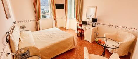 A bedroom with a bed, a desk, a chair, a small table with fruits, and a TV.