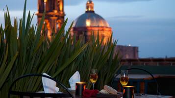 Una mesa con una copa de vino, una vela y una rosa, con vistas a una cúpula y un edificio al fondo.