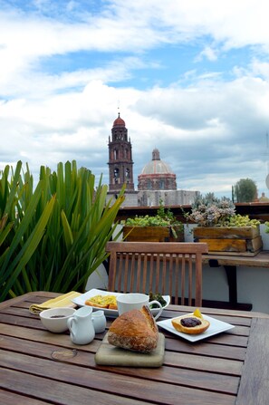 A wooden table with breakfast items, a view of a historic building with a bell tower and dome, and green plants in the foreground.