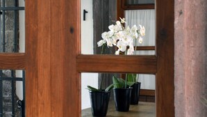 Una puerta de madera con un panel de vidrio, por donde se ven flores blancas y plantas en macetas.