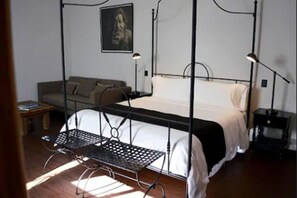 A bedroom with a bed, a chair, a nightstand, a lamp, a sofa, and a painting on the wall.