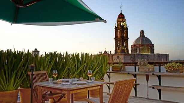 Una terraza con mesa y sillas, plantas en macetas y vistas a un edificio histórico con una torre de reloj y cúpula.