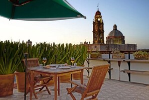 A terrace with a table and chairs, potted plants, and a view of a historic building with a clock tower and dome. - Casa de los Olivos (San Miguel de Allende)