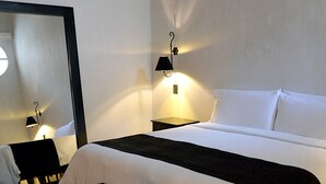 Habitación de hotel con una cama grande, una mesita pequeña, una mesita de noche con lámpara y un espejo en la pared.