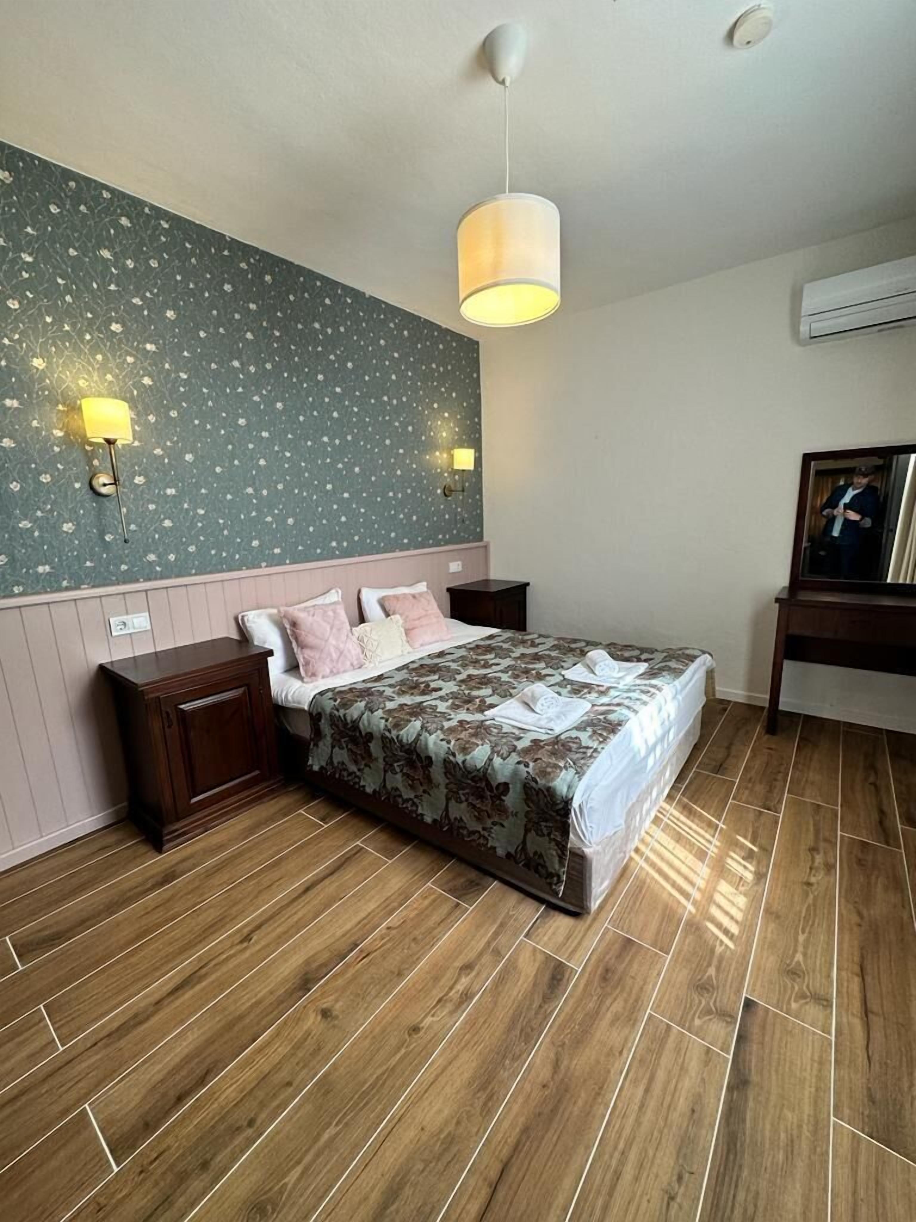 Un dormitorio con cama, piso de madera, luminarias fijadas a la pared y un espejo.
