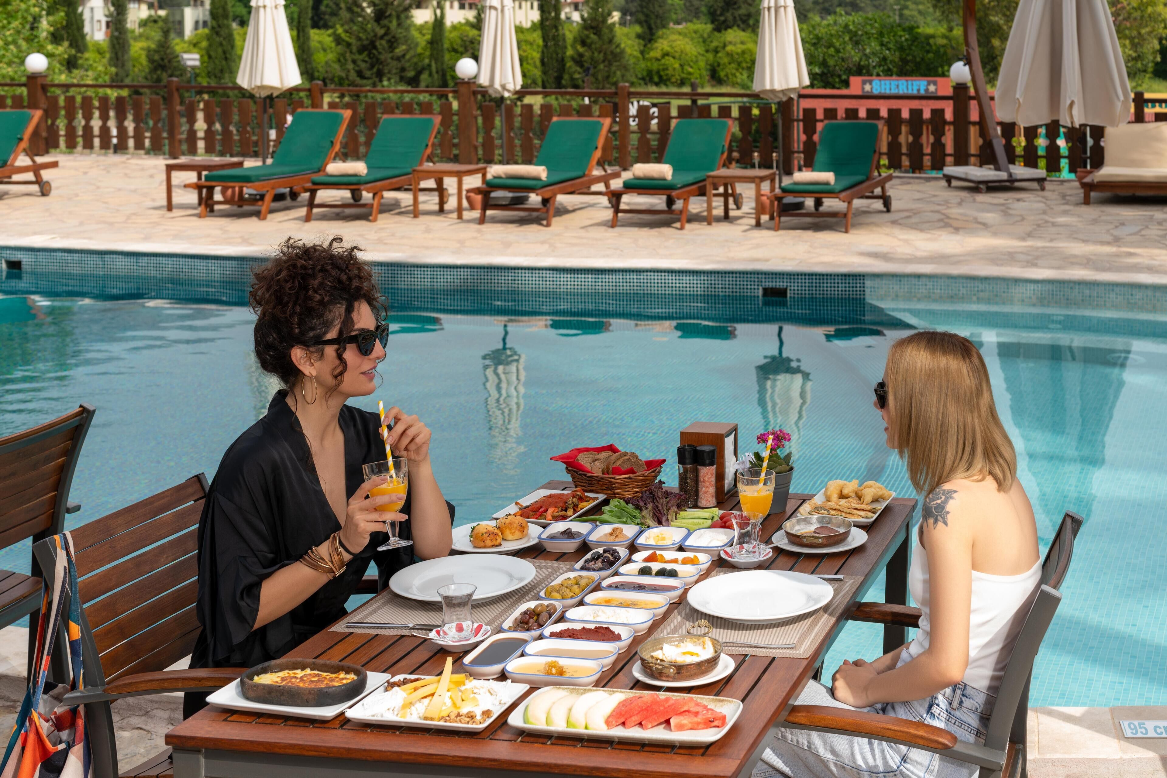A poolside dining area with a table set for two, surrounded by lounge chairs and a pool.