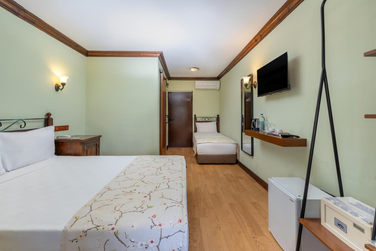 A hotel room with a large bed, a smaller bed, a TV mounted on the wall, a refrigerator, and a wooden nightstand.