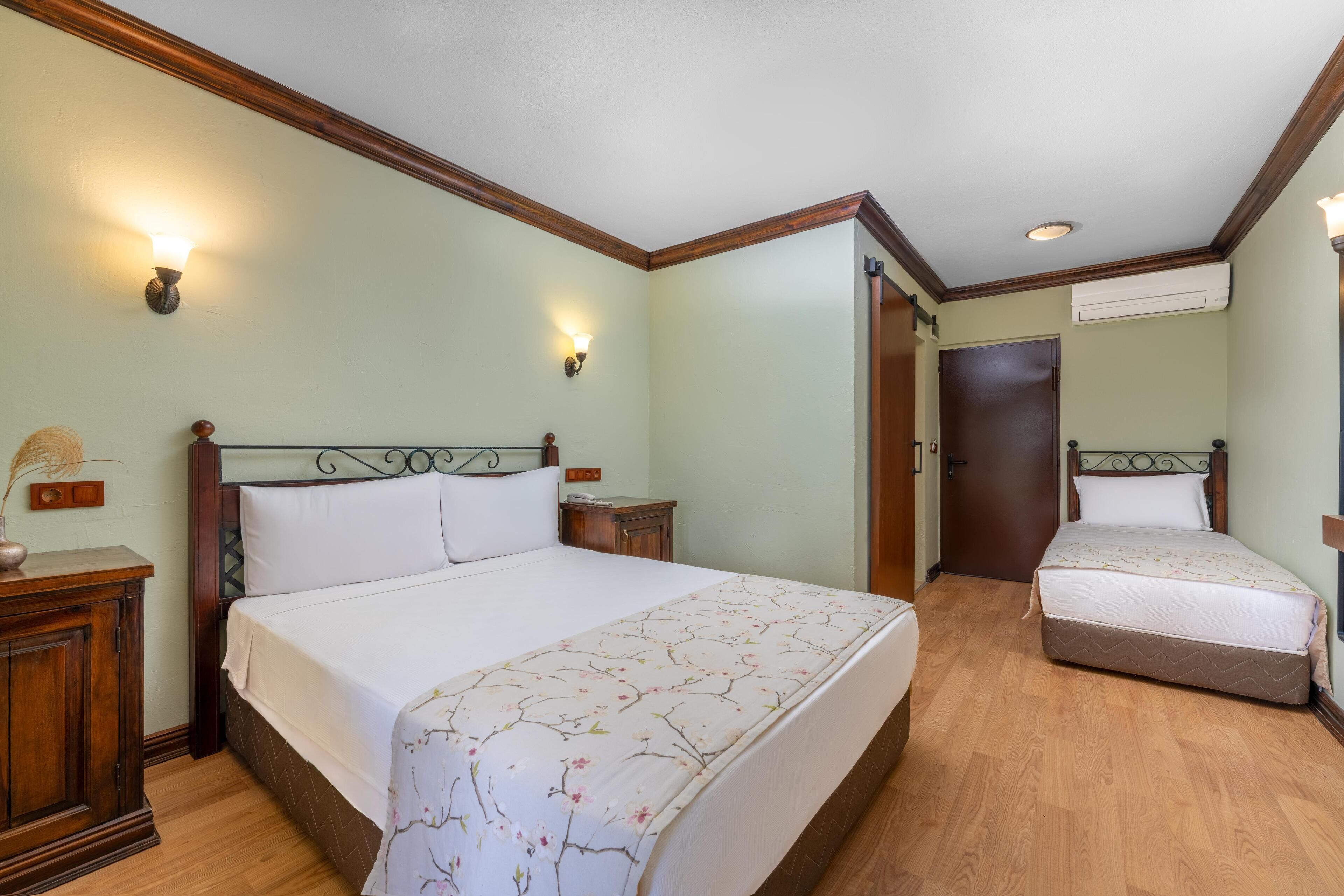Een hotelkamer met twee bedden, houten hoofdeinden, een nachtkastje met een lamp en een airconditioner aan de muur.