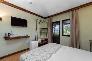 Habitación de hotel con cama, televisor montado, repisa con artículos de aseo, radiador y ventana con cortinas.