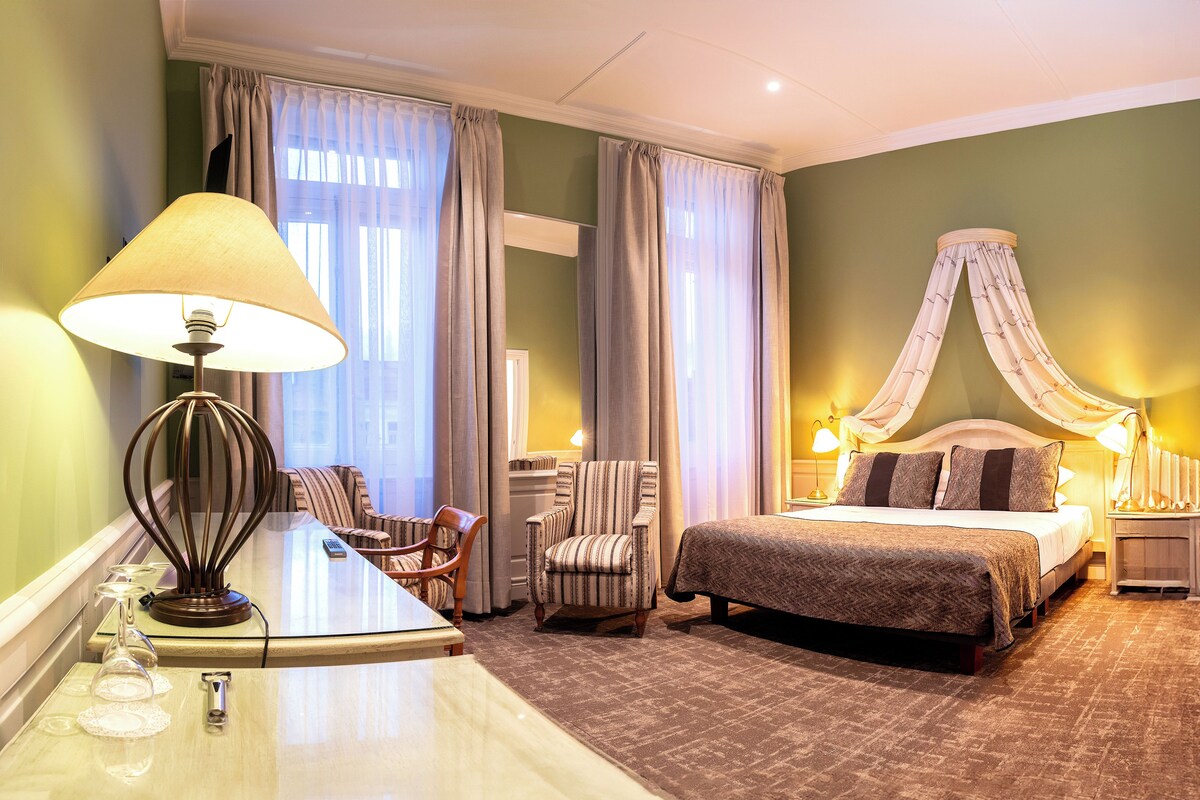 Ein Hotelzimmer mit einem Bett, einem Schreibtisch mit Lampe, einem Sessel und einem Nachttisch mit Lampe.