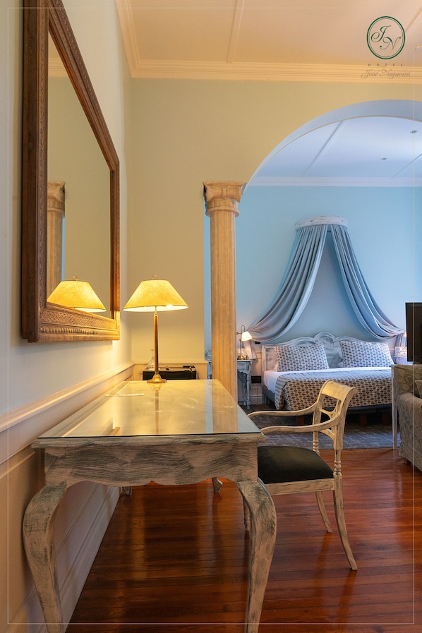 Quarto de hotel com cama, mesa de cabeceira, luminária, cadeira e espelho.