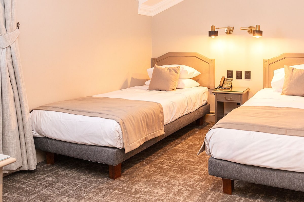 Ein Hotelzimmer mit zwei Einzelbetten, einem Nachttisch mit Lampe und einem an der Wand befestigten Telefon.