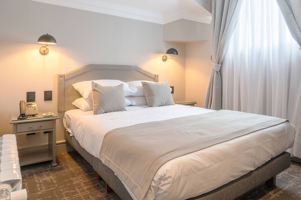 Ein ordentlich bezogenes Bett mit weißen Leinen, ein Nachttisch mit Lampe und ein Telefon.