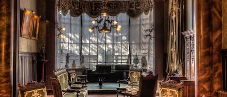 A grand room with ornate furniture, a grand piano, and a large window with intricate curtains.