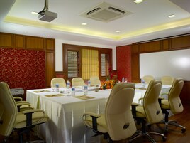 Une salle de conférence avec une longue table, des chaises de couleur beige et un projecteur fixé au plafond.