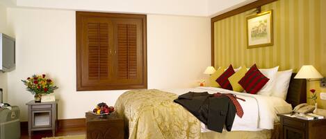 A hotel room with a large bed, a wooden wardrobe, a bedside table with a lamp, and a small table with a vase of flowers.