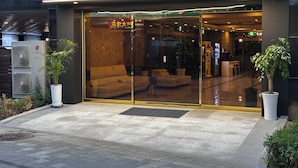 L’entrée d’un hôtel, avec une porte en verre, une enseigne indiquant « HÔTEL JUNE » et un espace salon à l’intérieur.