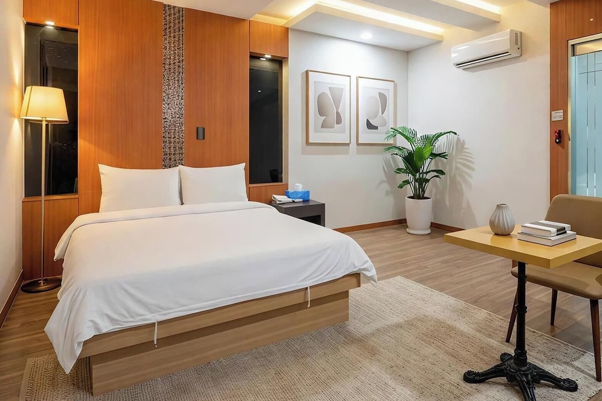 A modern hotel room with a wooden bed, a desk, a potted plant, and artwork on the walls.