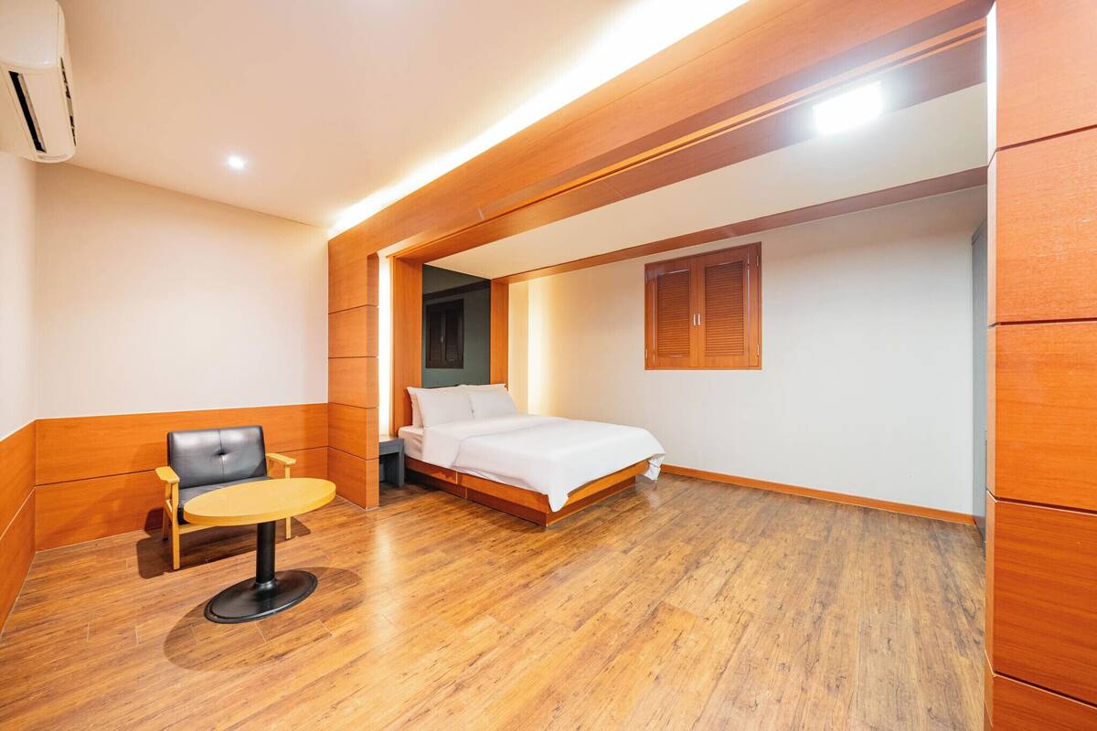 A modern hotel room with a wooden floor, a bed, a chair, and a small table.