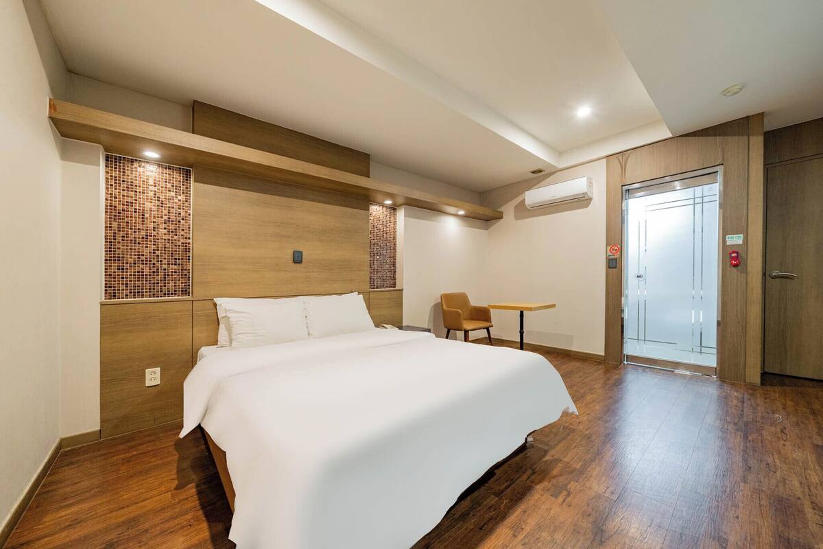A hotel room with a large bed, a small table, a chair, and a wardrobe.