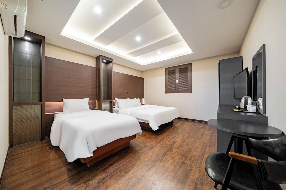 A hotel room with two beds, a desk, and a mirror.